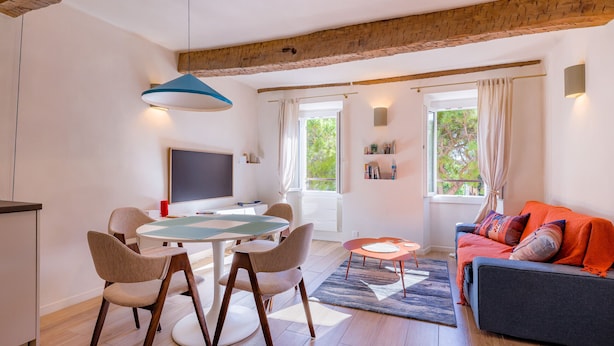Un soggiorno moderno con zona pranzo, pavimento in legno, un divano con cuscini, una TV e una finestra con tende.