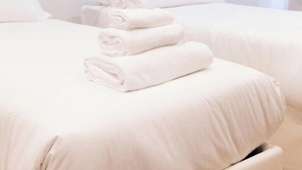 A hotel room with two beds, white bedding, a wall with a leaf pattern, and a white lamp.