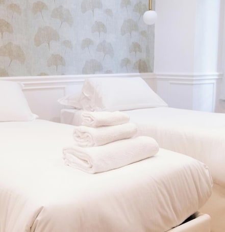 A hotel room with two beds, white bedding, a wall with a leaf pattern, and a white lamp.