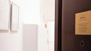 A hotel room with a wooden door, a white wall with a framed certificate, and a black umbrella leaning against the wall.