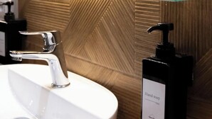 A bathroom with a white sink, a chrome faucet, a soap dispenser, and a glass shelf.