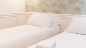 A hotel room with two single beds, white bedding, and a floral wallpaper pattern.