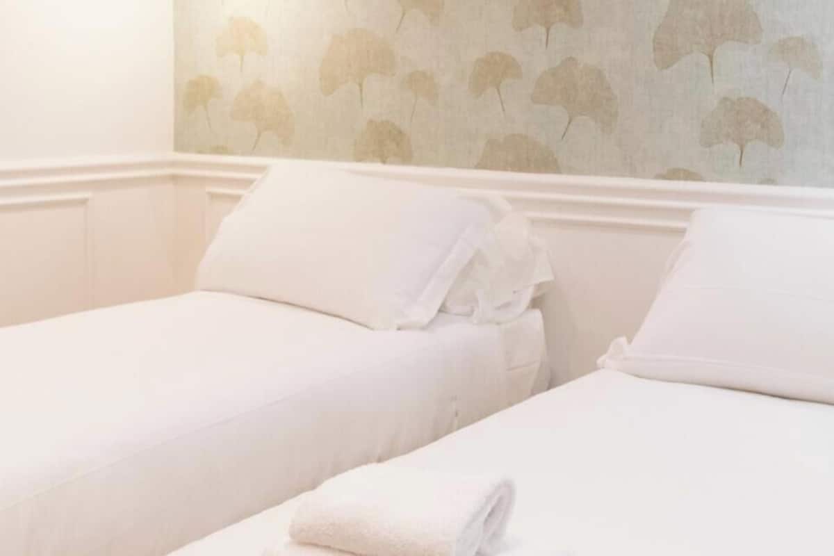 Una habitación de hotel con dos camas individuales, ropa de cama blanca y un estampado de papel tapiz floral.