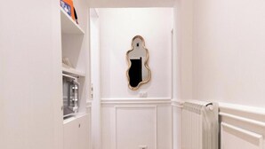 A narrow hallway with white walls, a wooden floor, a radiator on the right, and a mirror on the wall.