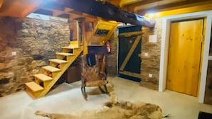 Tunnelmallinen sisustus, jossa on kiviseinä, puinen portaikko ja suuri turkismatto lattialla.