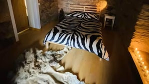 Makuuhuoneessa on seepramarmorikuviollinen sänky, kiviseinä, ovi ja pieni yöpöytä, jossa on lamppu.