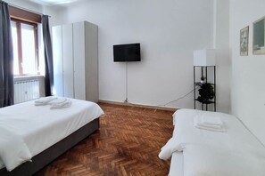 Una camera d'albergo con due letti, una TV a parete, un termosifone e un pavimento in legno.