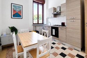 Een moderne keuken met een eettafel, stoelen, een radiator, een raam en een lijst met een foto aan de muur.