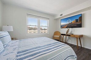 Ein Hotelzimmer mit Bett, Schreibtisch, Stuhl, Fernseher und einem Fenster mit Blick auf Gebäude.