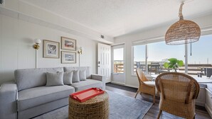 A living room with a grey sofa, wicker ottoman, wicker chair, and a red tray. - Immaculant One Bedroom Condo, Conveniently Located On 40th ST (Ocean City)
