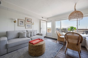 Ein Wohnzimmer mit grauem Sofa, Ottomane aus Rattangeflecht, Rattanstuhl und einem roten Tablett.