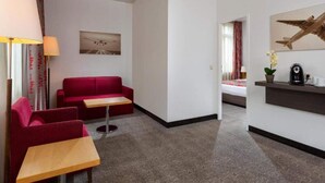 A hotel room with a red sofa, a small wooden table, a bed with a red and white bedspread, a wall-mounted airplane decoration, and a small potted plant. - 4 Person Holiday Park Home in Neu-isenburg (Neu-Isenburg)
