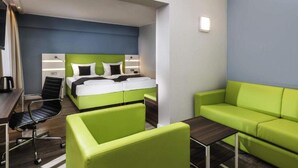 A hotel room with a bed, a desk, a chair, and a green sofa. - 4 Person Holiday Park Home in Offenburg (Offenburg)