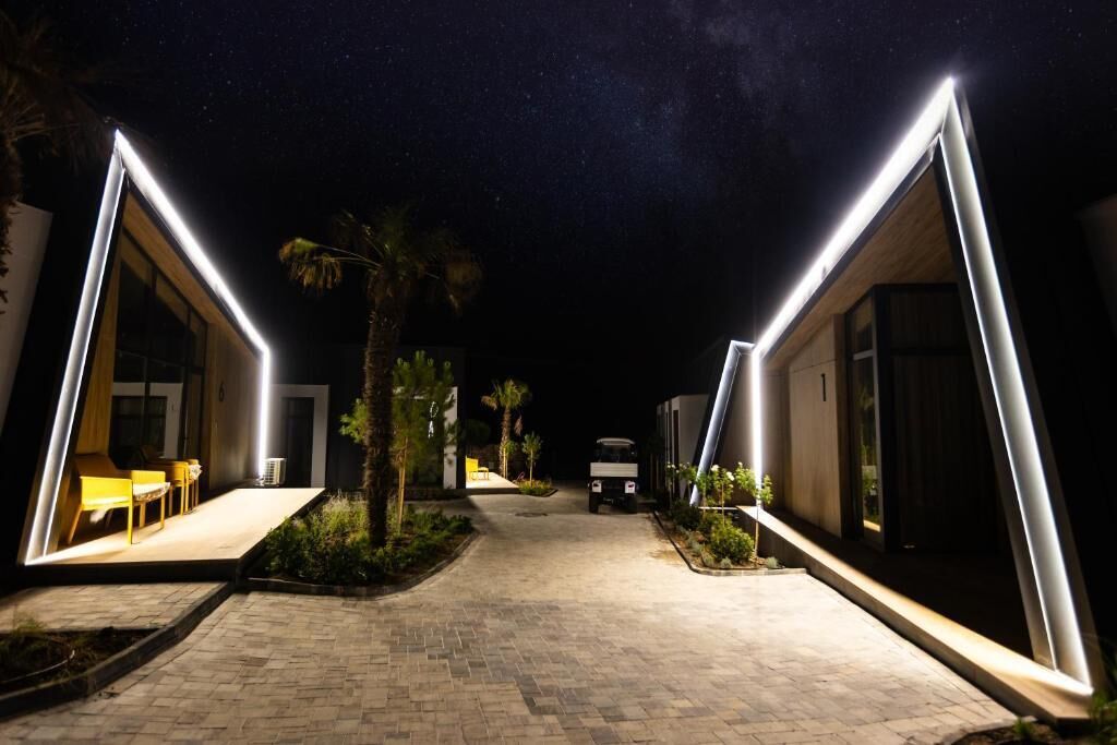 Een pad dat leidt naar een gebouw met verlichte randen, een voertuig geparkeerd ervoor en een kleine tafel met stoelen buiten.