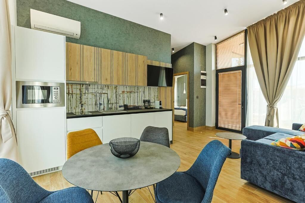 A modern kitchen with a microwave, stove, and wooden cabinets. There is a dining area with a round table and blue chairs.