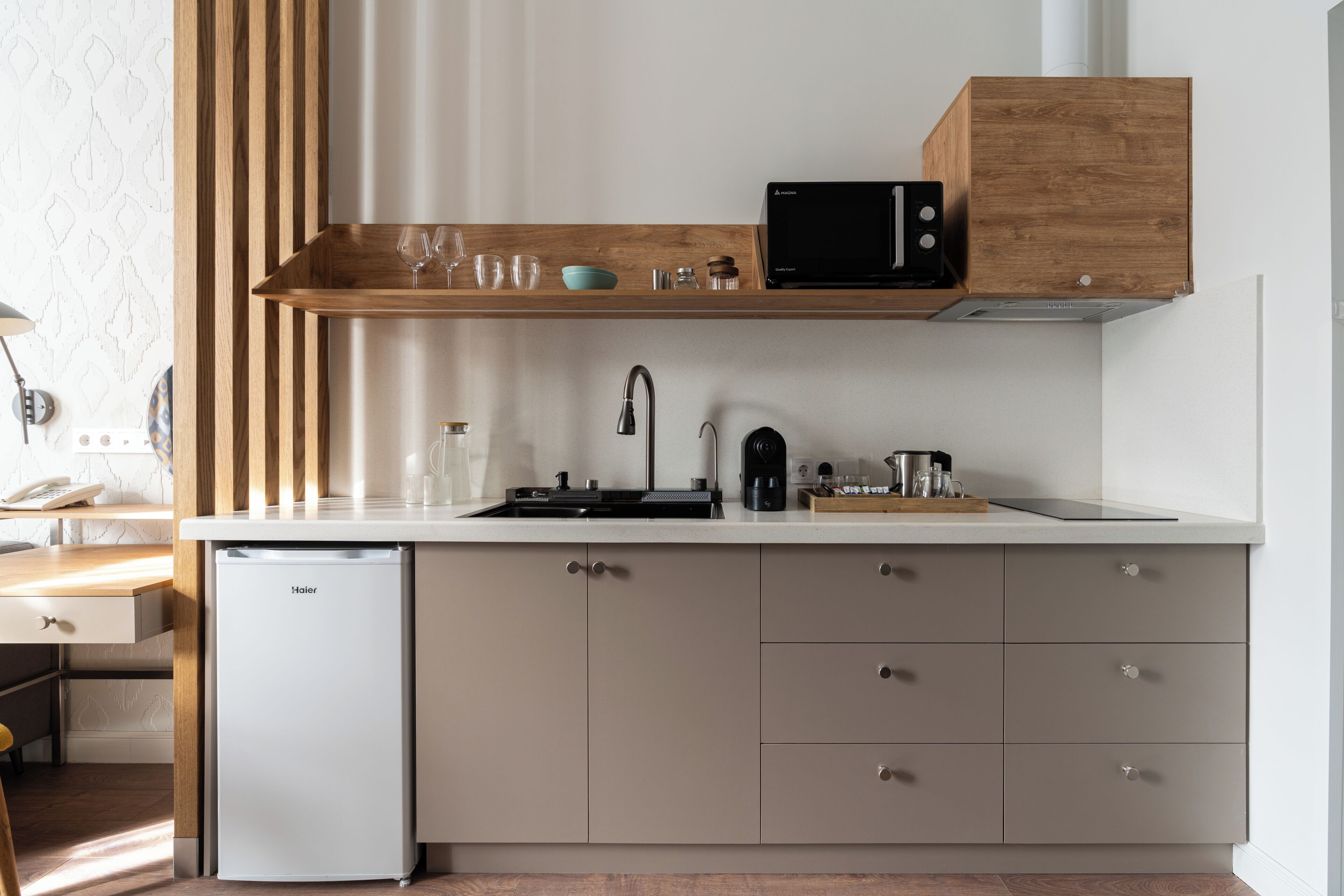A compact kitchen with a built-in dishwasher, a microwave, and a wooden shelf above the sink.