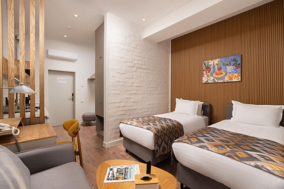 A hotel room with two beds, a desk with a telephone, a chair, a coffee table with a magazine, and a painting on the wall.