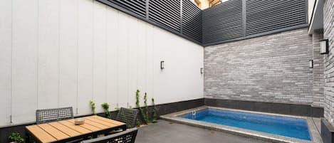 A patio with a pool, a table, and chairs.