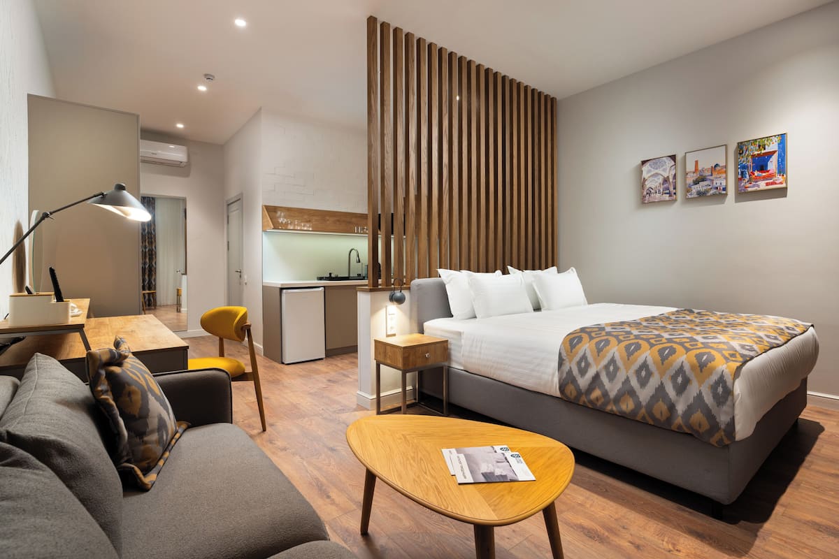 A modern hotel room with a bed, a desk, a chair, a small table, and a sofa.