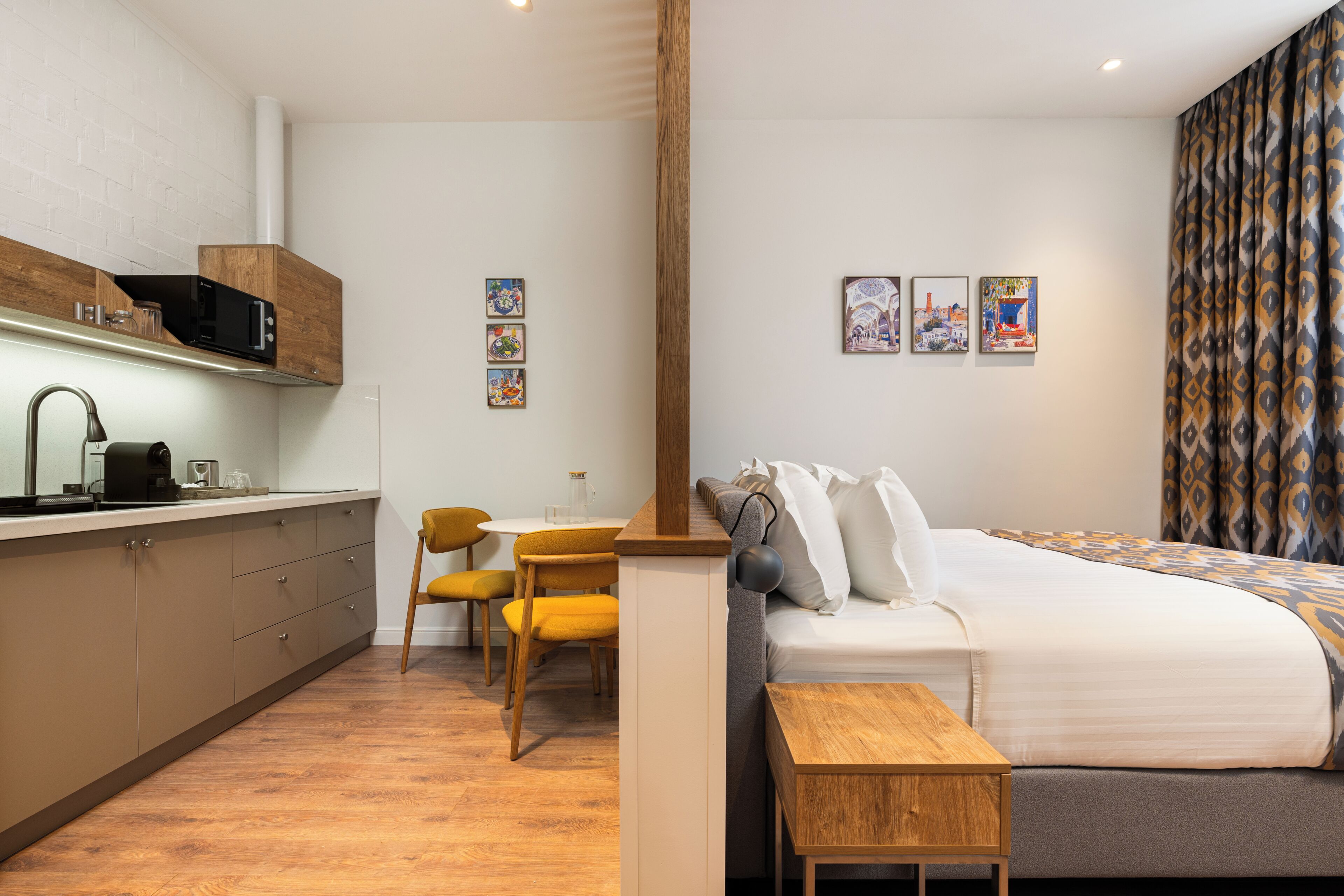 A modern hotel room with a kitchenette, a bed, a dining area, and artwork on the walls.