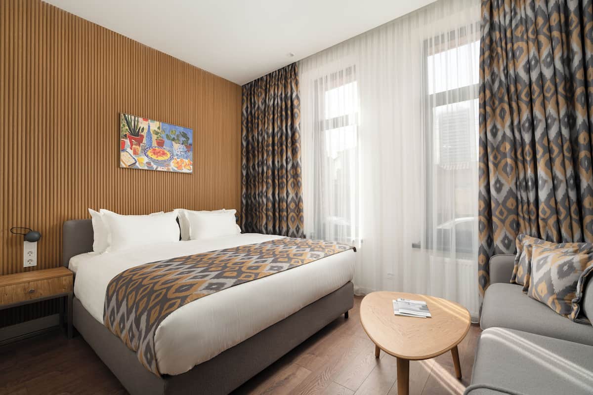 A hotel room with a bed, a sofa, a small table, and a painting on the wall.