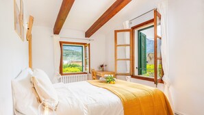 A bedroom with a bed, a bedside table with a lamp, a window with a view of greenery, and a wooden ceiling. - Holiday Home 'Ca N'Antonia' citrus farm stay (Sóller)