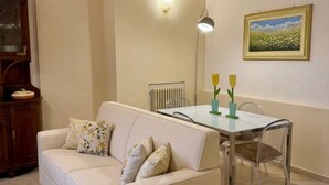 Ein Wohnzimmer mit einer Couch, einem Esstisch mit Stühlen, einem Heizkörper und einer Wandleuchte.