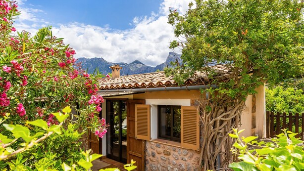 Una casa de piedra con techo de tejas, contraventanas de madera y vistas a las montañas.