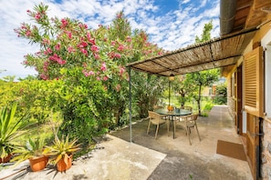 Un patio con una mesa y sillas, rodeado de plantas en macetas y una pérgola.