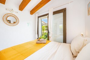 Un dormitorio con cama, techo de madera, ventana con cortinas y espejo adosado a la pared.