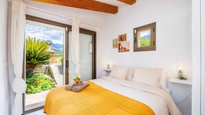 Un dormitorio con cama, una ventana con cortinas, una mesita de noche con lámpara y vistas al exterior.