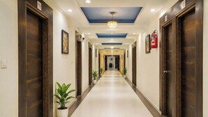 A hotel corridor with wooden doors, potted plants, and a blue ceiling. - Hotel Apollo SpRing Road Odhav Ahemdabad (Ahmedabad)
