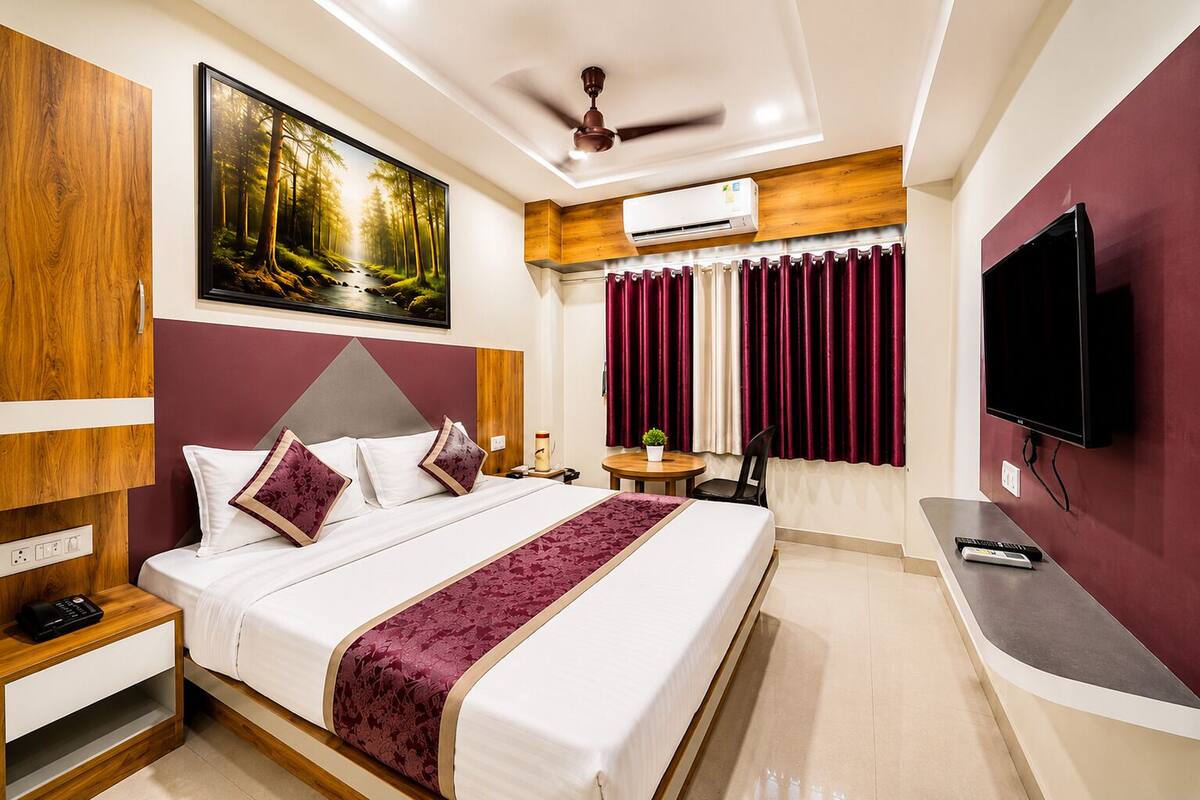 Ein Hotelzimmer mit Bett, Schreibtisch, Fernseher, Klimaanlage und einem Waldgemälde.
