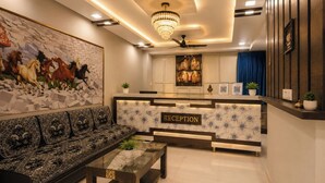 A reception area with a sofa, a coffee table, a chandelier, a ceiling fan, and a wall with a horse painting. - Hotel Apollo SpRing Road Odhav Ahemdabad (Ahmedabad)
