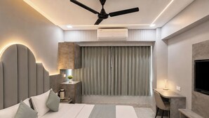A modern hotel room with a bed, desk, chair, and a ceiling fan. - Hotel Apollo SpRing Road Odhav Ahemdabad (Ahmedabad)