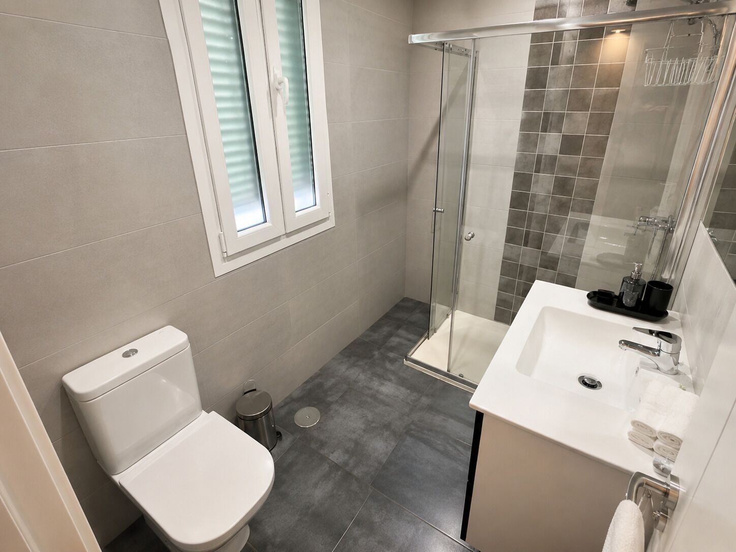 A modern bathroom with a toilet, a glass shower enclosure, and a sink with a mirror.