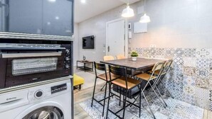 Kompakti keittiö, jossa on sisäänrakennettu uuni, pesukone, ruokailutila pöydän ja tuolien kera sekä kuvioituja laattoja seinissä.