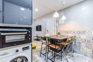 A compact kitchen with a built-in oven, a washing machine, a dining area with a table and chairs, and patterned tiles on the walls. - Retiro V (Madrid)
