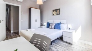 Moderni hotellihuone, jossa on sänky, yöpöytä ja työpöytä tuolilla.