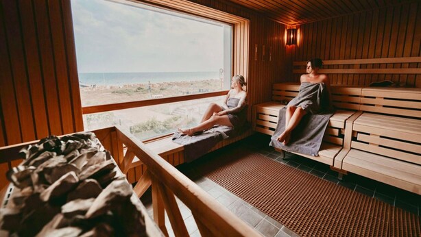 A sauna room with wooden benches and a large window overlooking a beach. - Ferienhaus fur Zwei mit Landlichem Charme (Fehmarn)