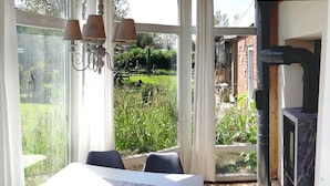 A conservatory with a table and chairs, a fireplace, and a view of a garden. - Ferienhaus fur Zwei mit Landlichem Charme (Fehmarn)
