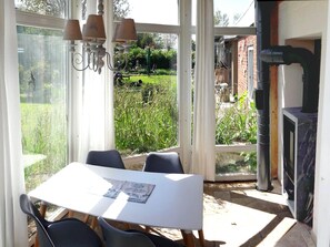 Ein Wintergarten mit Tisch und Stühlen, einem Kamin und Blick auf einen Garten.