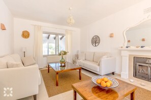 Ein Wohnzimmer mit einer Couch, einem Couchtisch, einem Kamin und einem Fenster mit Vorhängen.