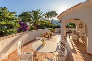 Eine Terrasse mit einem runden Tisch und Stühlen, umgeben von Topfpflanzen und Blick auf das Meer.