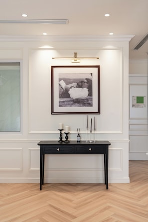 A hallway with a framed photograph, a dark console table with candles, and a light fixture above. - AN Hotel & Residence (Ha Noi)
