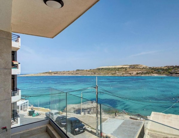 Ein Balkon mit freiem Blick auf das Meer, ein geparktes Auto und eine entfernte Küstenlinie.