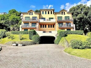 A multi-story residential building with a central entrance, balconies, and a landscaped driveway. - Elegant modern apartment with pool and panoramic balconies (Stresa)
