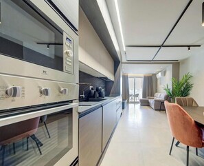 A modern kitchen with built-in appliances, a dining area with a table and chairs, and a living space with a sofa and a plant. - A Stylish 2BR seafront home in Qawra w/WIFI & AC (San Pawl il-Baħar)