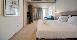 A modern hotel room with a large bed, a potted plant, a view of the city, and a large abstract painting on the wall. - A Stylish 2BR seafront home in Qawra w/WIFI & AC (San Pawl il-Baħar)