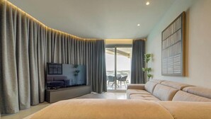 A modern living room with a large sofa, a flat-screen TV, and a balcony with a table and chairs. - Seafront Seafront 3BR home in Qawra w/WIFI & AC (San Pawl il-Baħar)